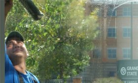 Commercial window cleaning by man in blue shirt using squeegee, cleaning GVSU building, downtown Grand Rapids, MI